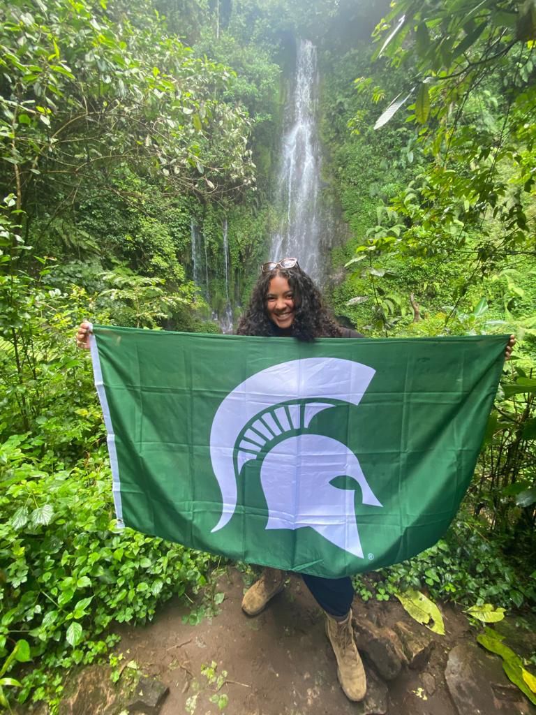 Helayne holding Spartan flag in front of waterfall