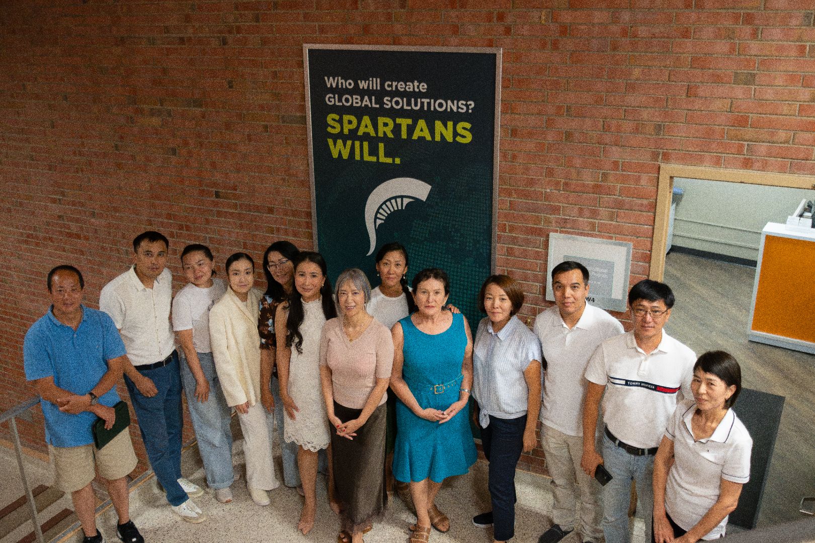 A group photo of Bolashak scholars, Dr. Chen and Dr. Wu in front of the VIPP Office post that reads, "Who will create global solutions? Spartans Will." with a spartan-head below. 