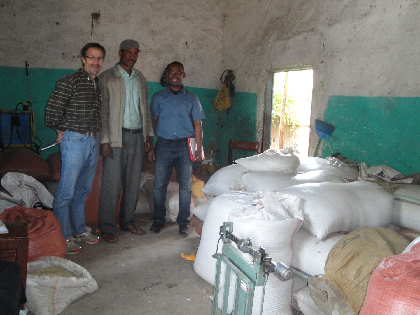Three smiling people stand in a concrete building in front bags of grain.