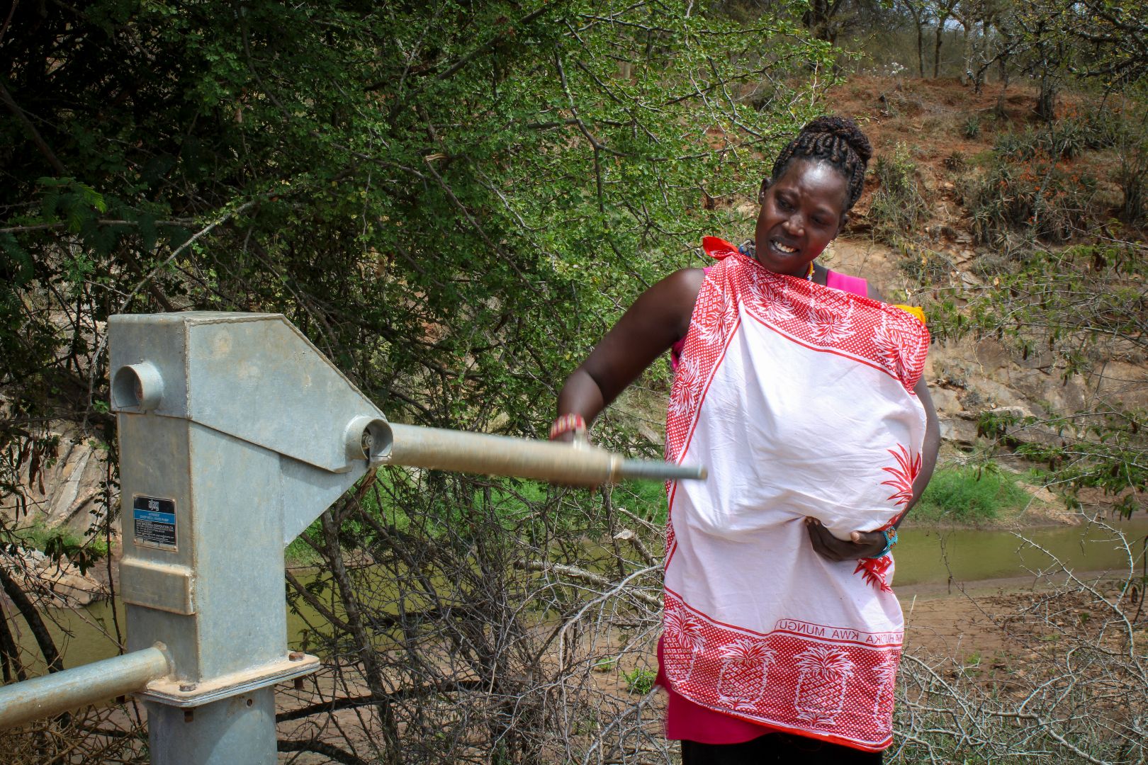 Kenyan woman holding baby in dress while at water pump station