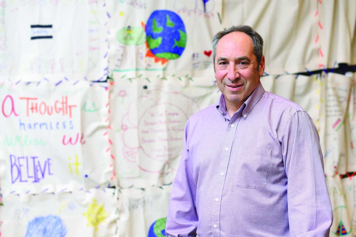 Robert Lurie stands in front of a white backdrop with hand-painted words.