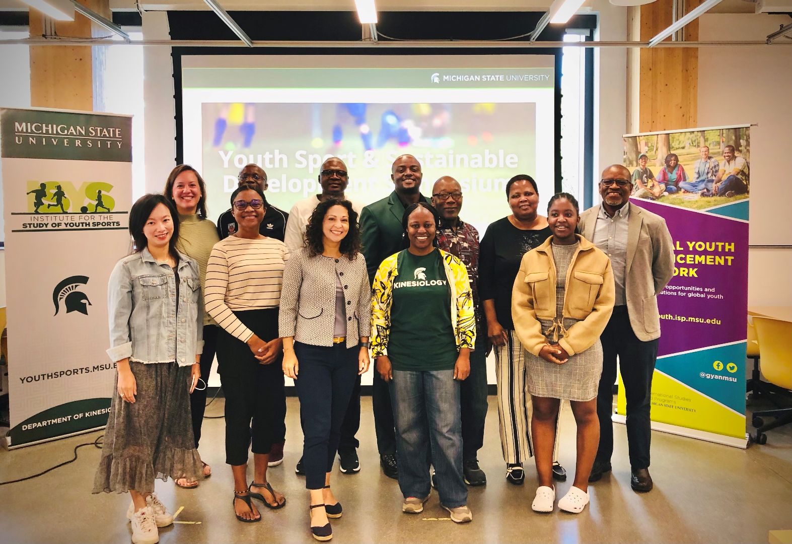 A group of participants and presenters stand posing for the camera in a classroom with ISYS and GYAN banners on either side of them