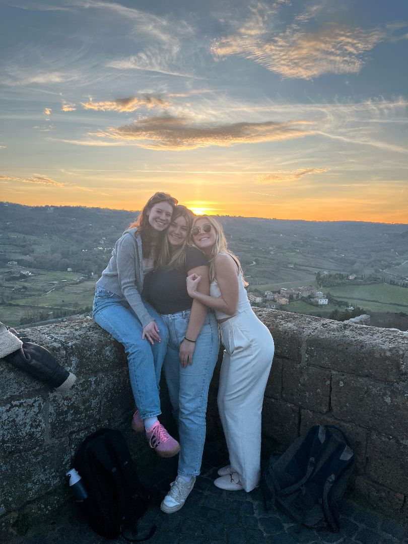 Greta and friends sitting on stone wall overlooking Italian countryside at sunset