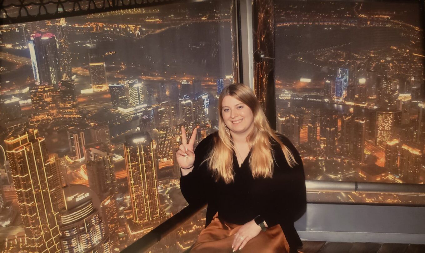 Courtney giving a peace sign sitting at the top of the Burj Khalifa at night