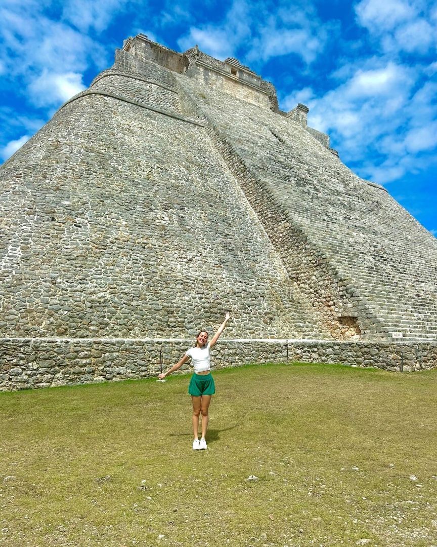 Maya standing in front of a Mayan ruin with her left arm raised high