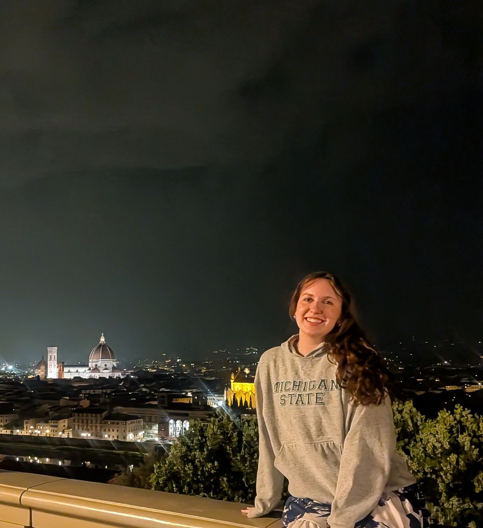 Oranna sitting on a stone wall at night with Florence in the background