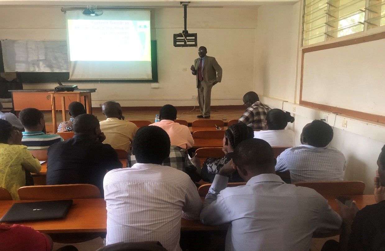 John B Kaneene stands at the front of a classroom presenting.