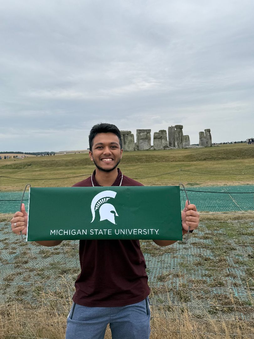 Dev holding an MSU banner in front of Stonehenge