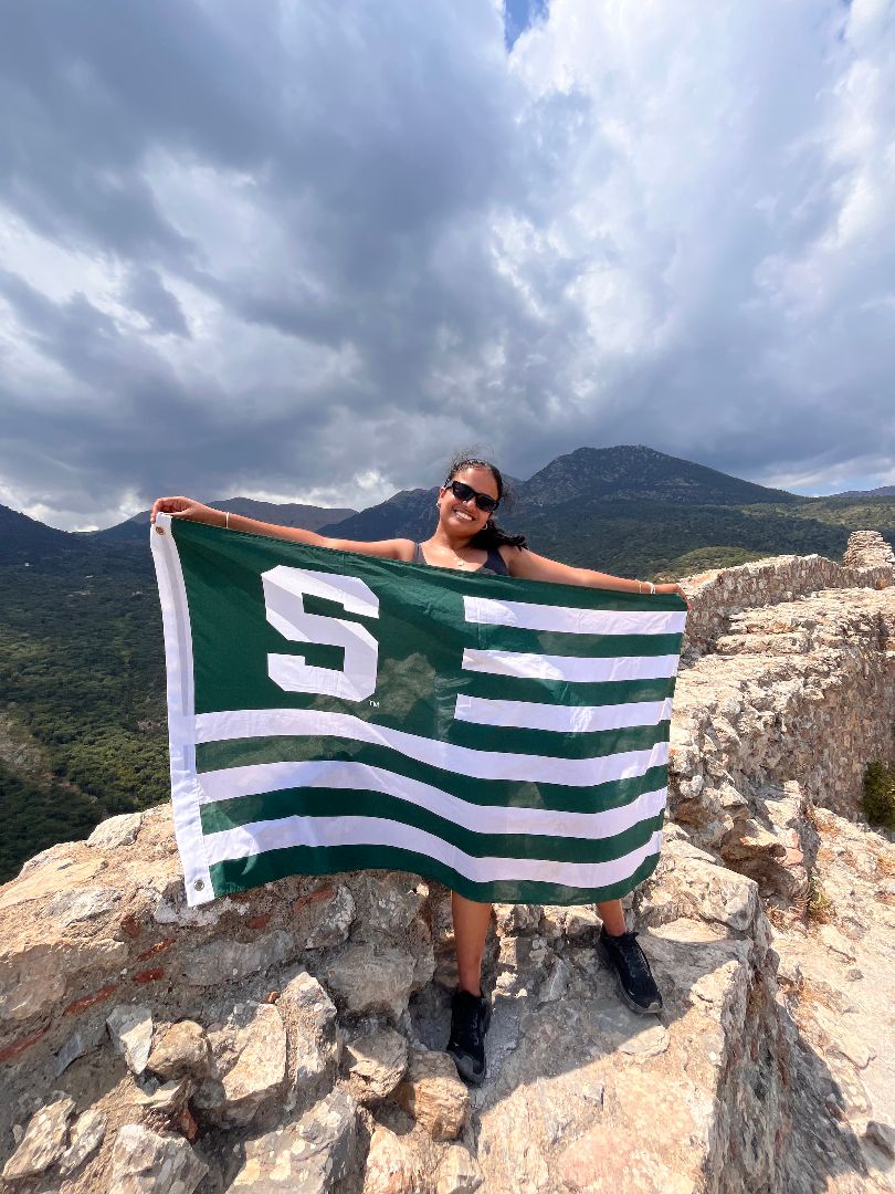 Shreya holding a Spartan flag on top of a mountain in Greece