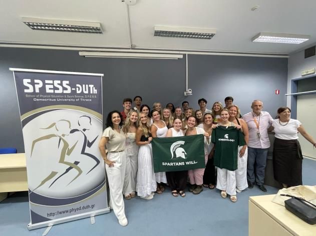 Group of students holding a Spartan flag and Spartan tee shirt in a classroom in Greece