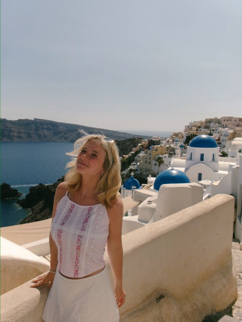 Anna wearing a white dress on a stone balcony in Santorini Greece