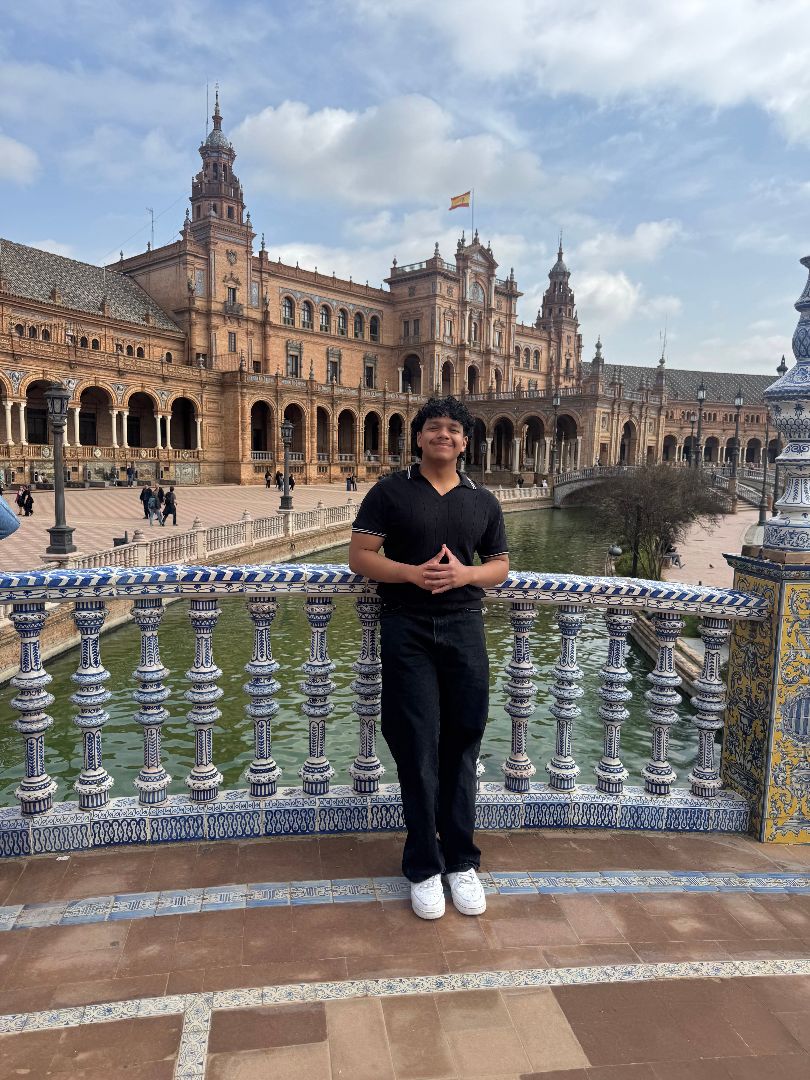 Mario wearing a black shirt and black pants standing on a small bridge over a canal in Spain