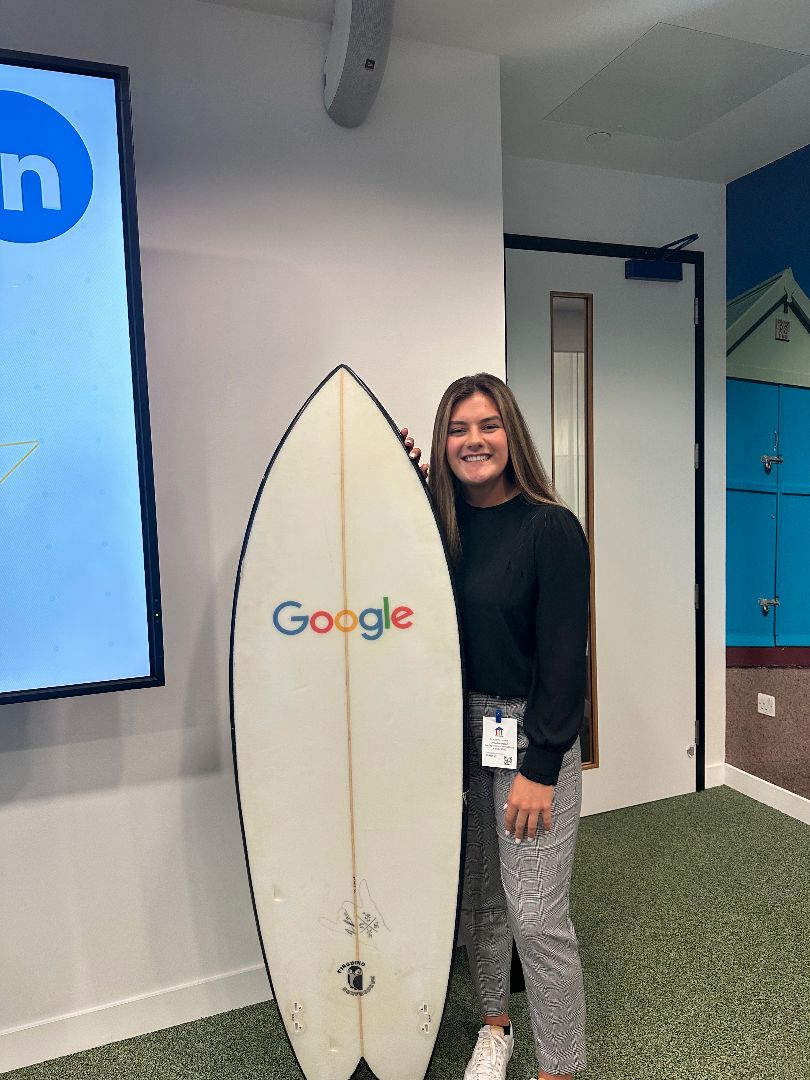 Anna standing with a surfboard branded by Google
