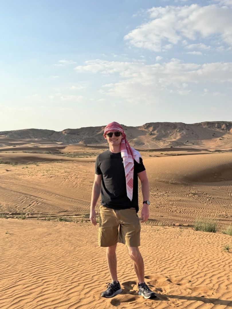 Raymond wearing a red and white headscarf standing in the desert in the UAE