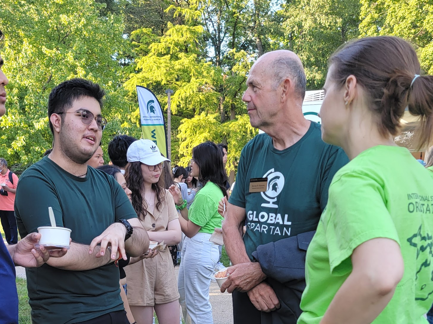 three people in casual clothing chat outside on a sunny day