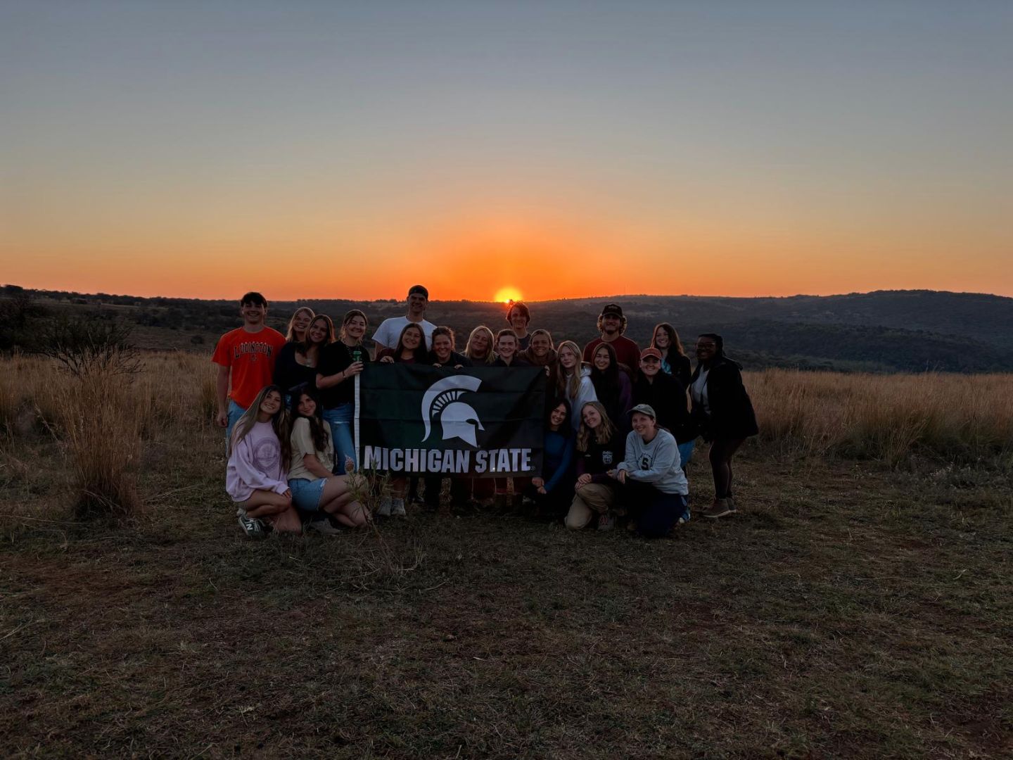 Group of students holding a Spartan flag in the savanah during sunset