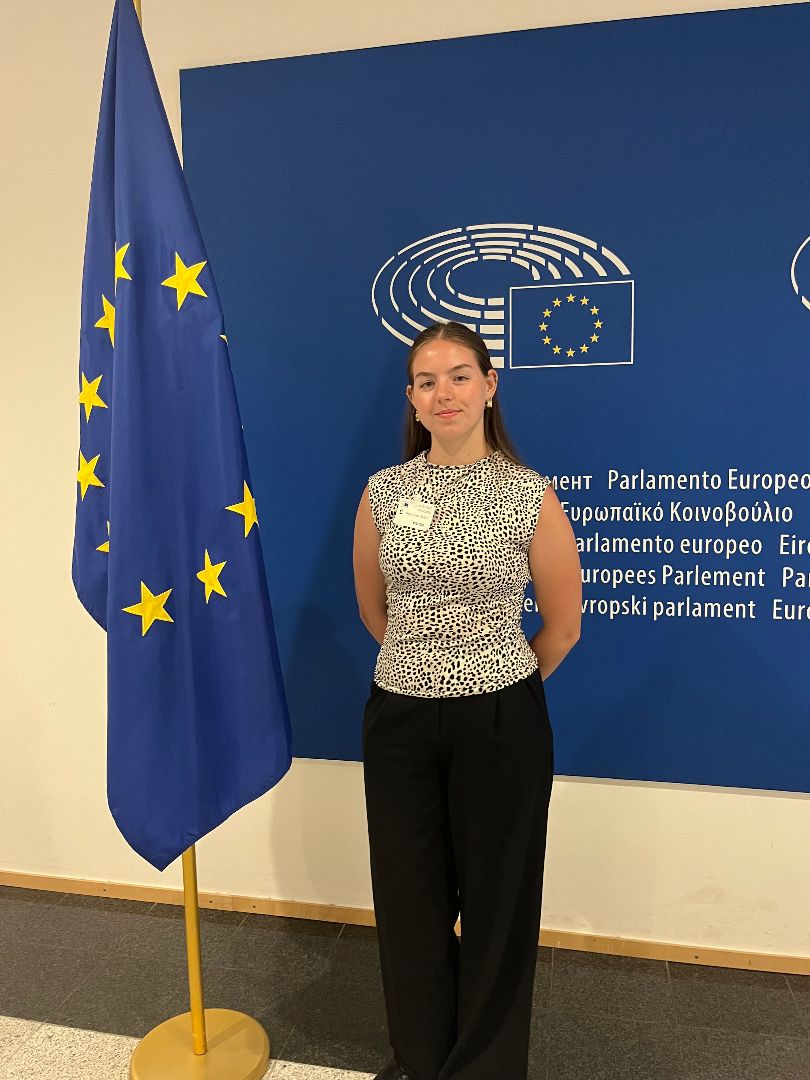 Riley standing next to the blue European Parliament flag