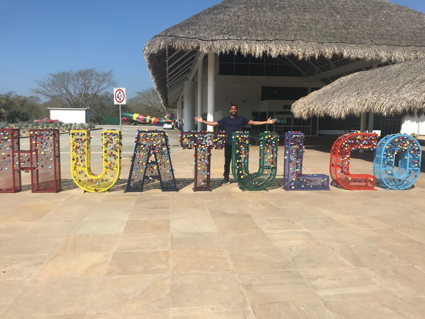 Johnson stands behind large metal letters that spell "HUATULCO"