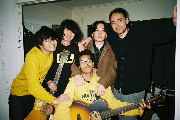 Five Japanese and U.S. students together, with two in the front holding acoustic guitars