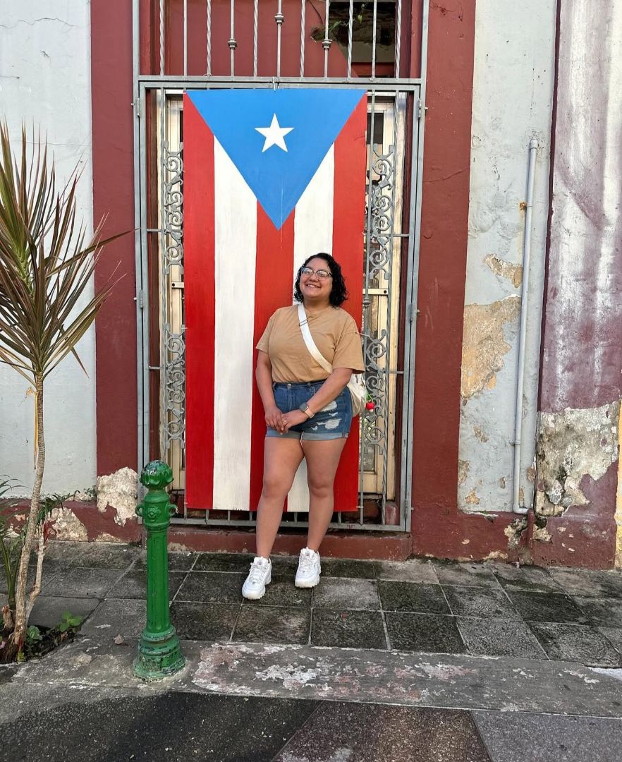 Alexis standing in front of a door draped with a Puerto Rican flag