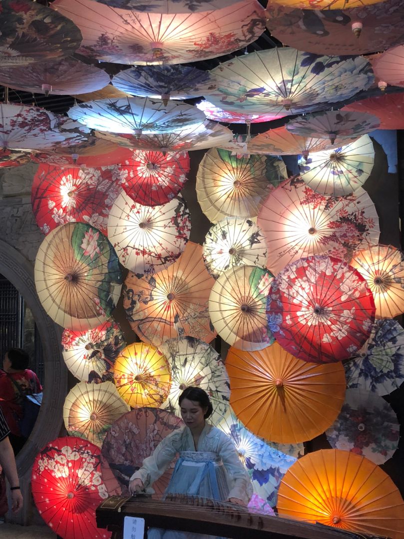 Multi-color paper umbrellas with different designs fill a space with a woman standing in the center.