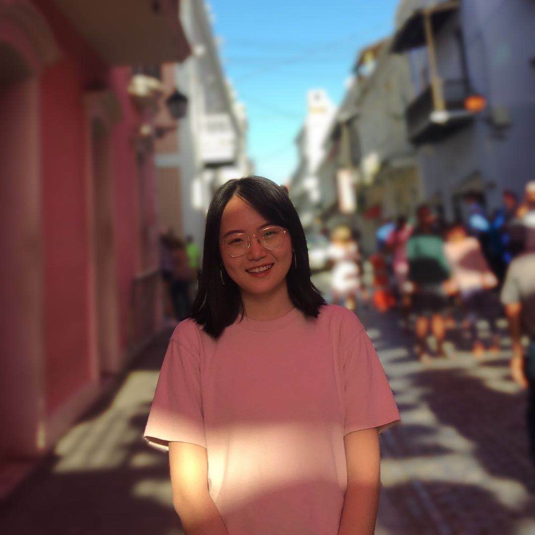 Melody stands smiling and in focus with a blurry city street scene behind her.