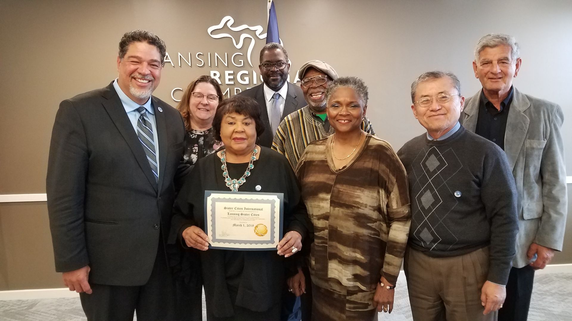 Sung Lee stands with Lansing Chamber of Commerce colleagues holding a plaque