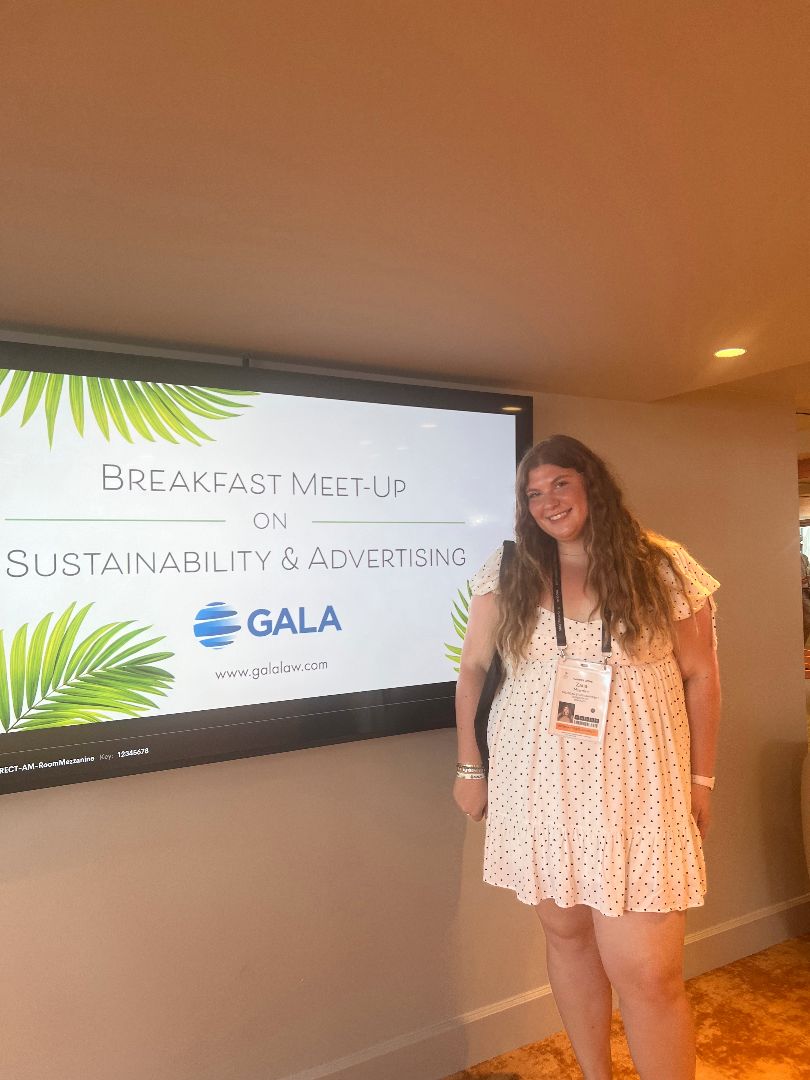 Zana standing in front of a video screen that says Breakfast Meet-up on Sustainability and Advertising