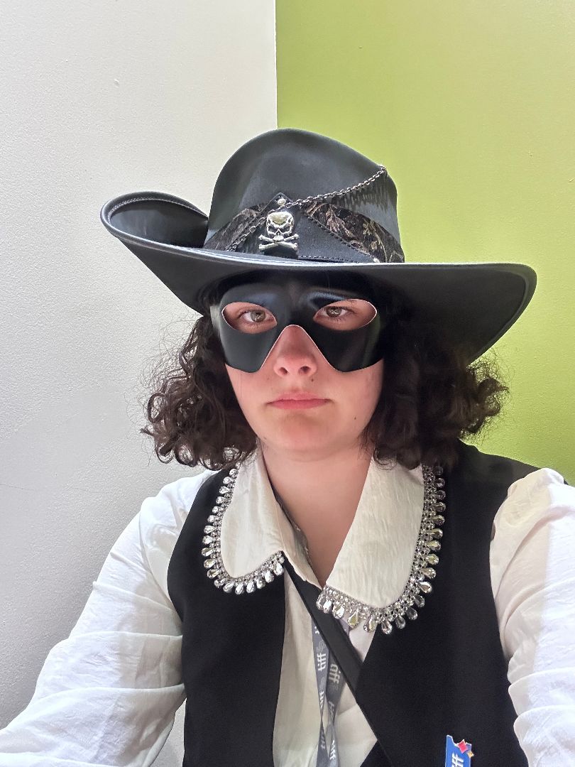 Addyson wearing a black hat, black mask and white shirt with black vest